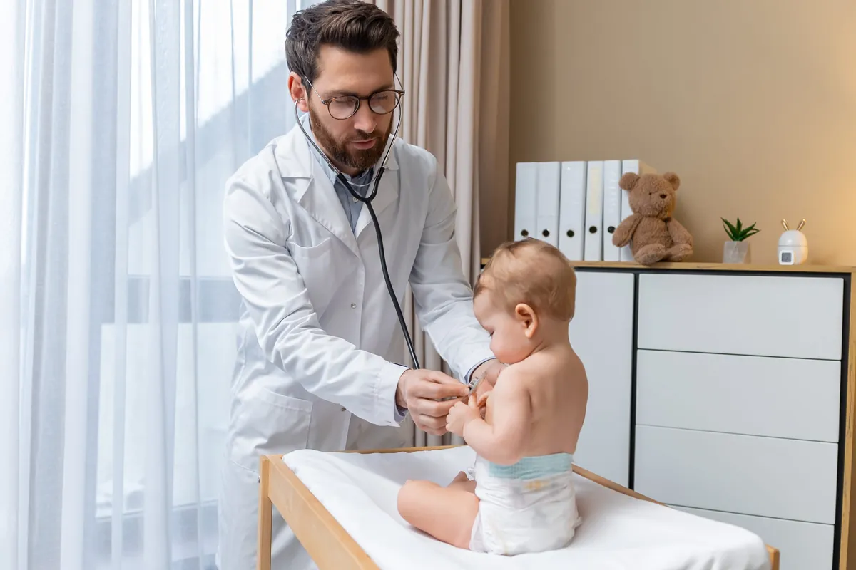 Pediatrician listening to a baby’s chest with a stethoscope on an exam table