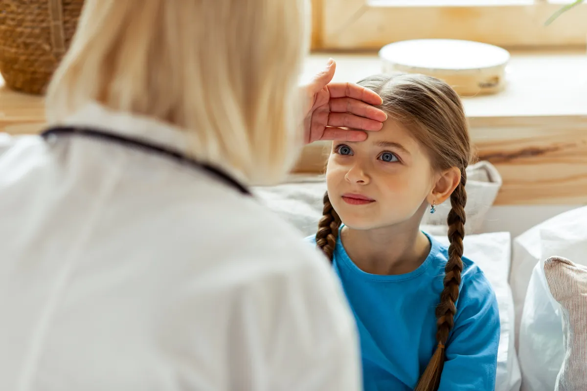 Pediatrician checking the forehead of a young girl with braided hair