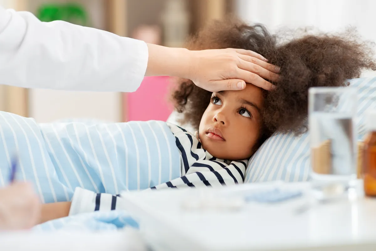 Provider gently checking the forehead of a young girl resting in bed