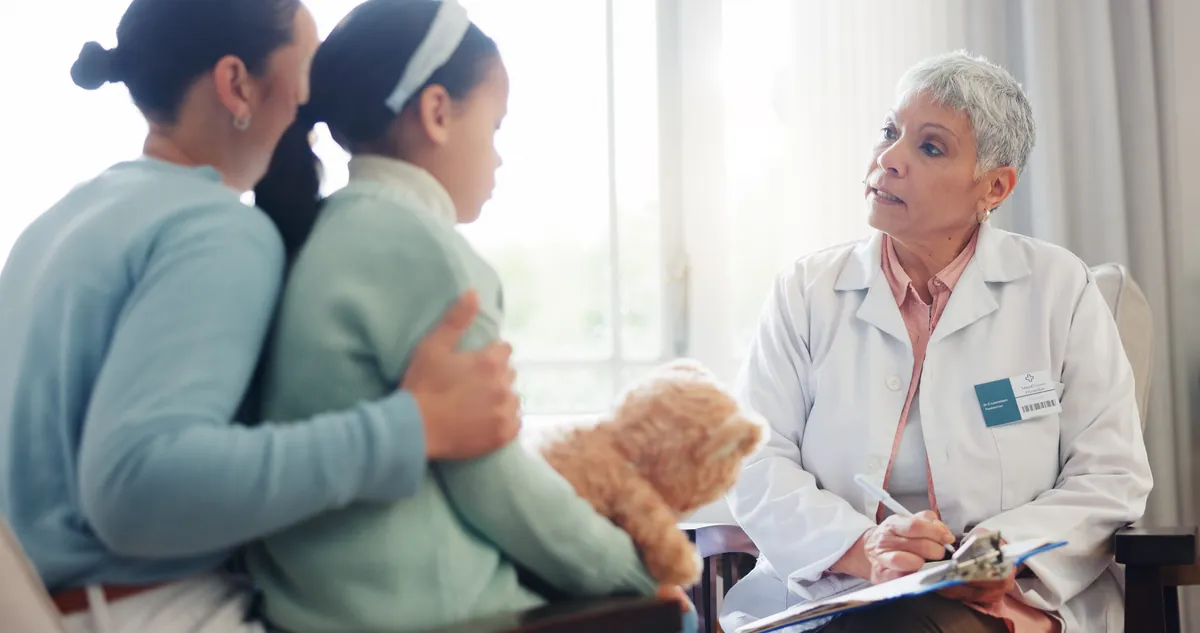 Mother hugging her daughter while a pediatrician takes notes during a visit