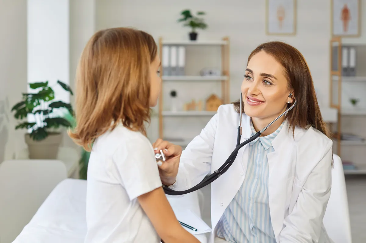 Smiling pediatrician listening to a young girl’s back with a stethoscope