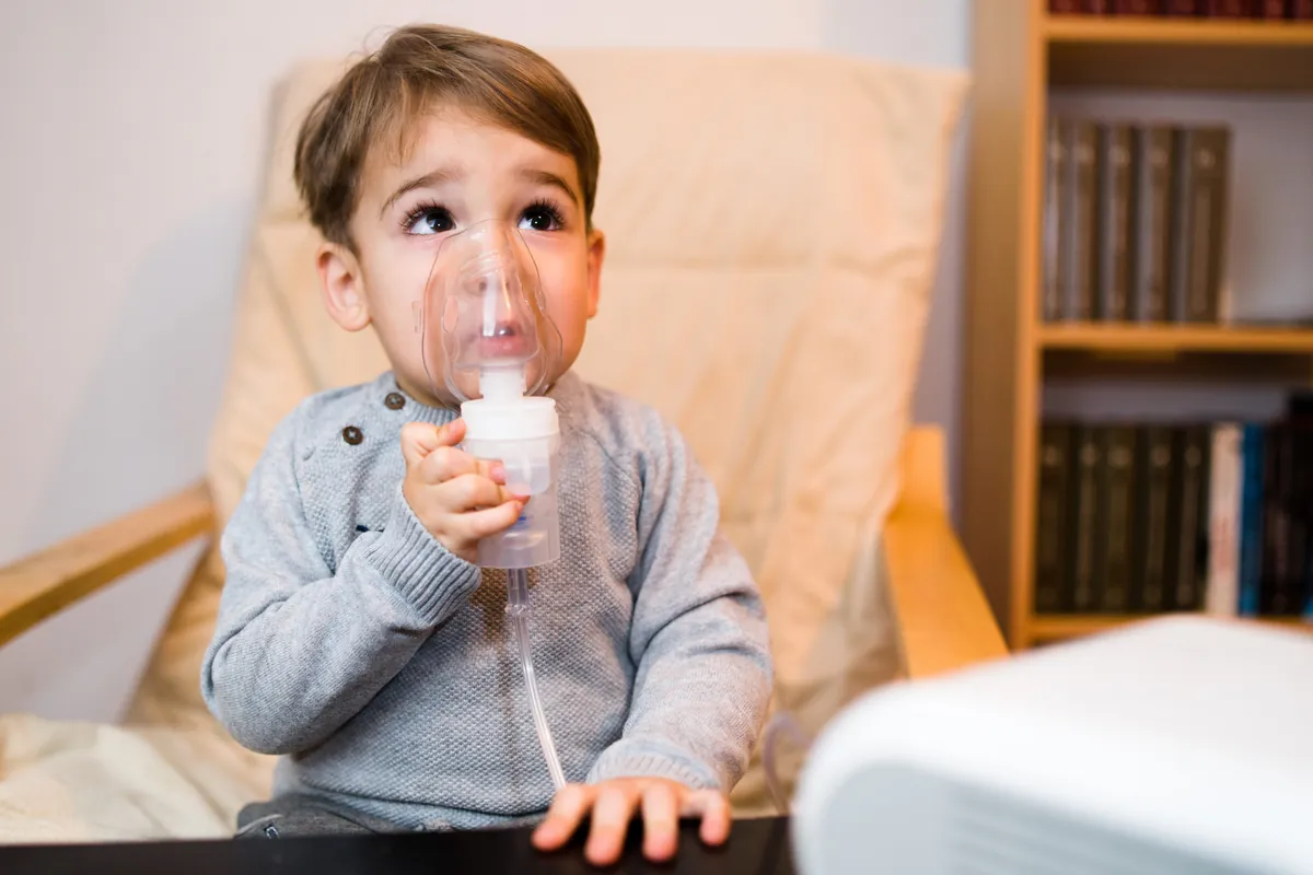 Toddler holding a nebulizer mask during a breathing treatment