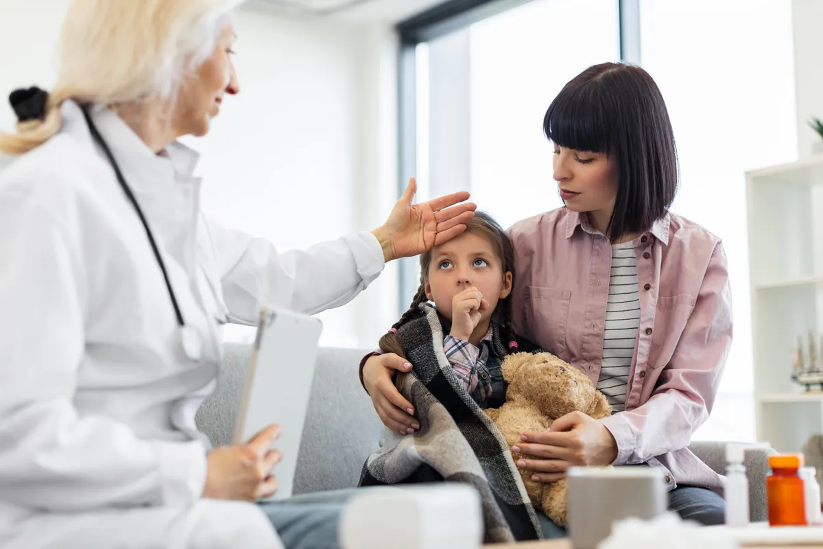 Doctor comforting a young child sitting in her mother’s lap